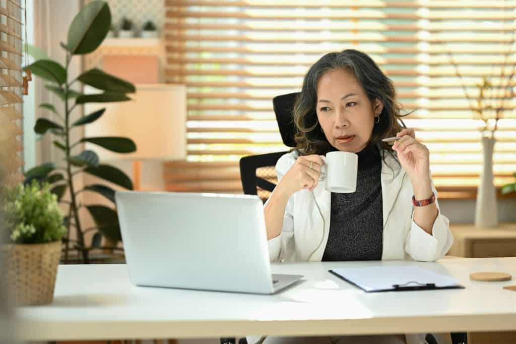 Senior businesswoman drinking coffee and watching online webinar during working online