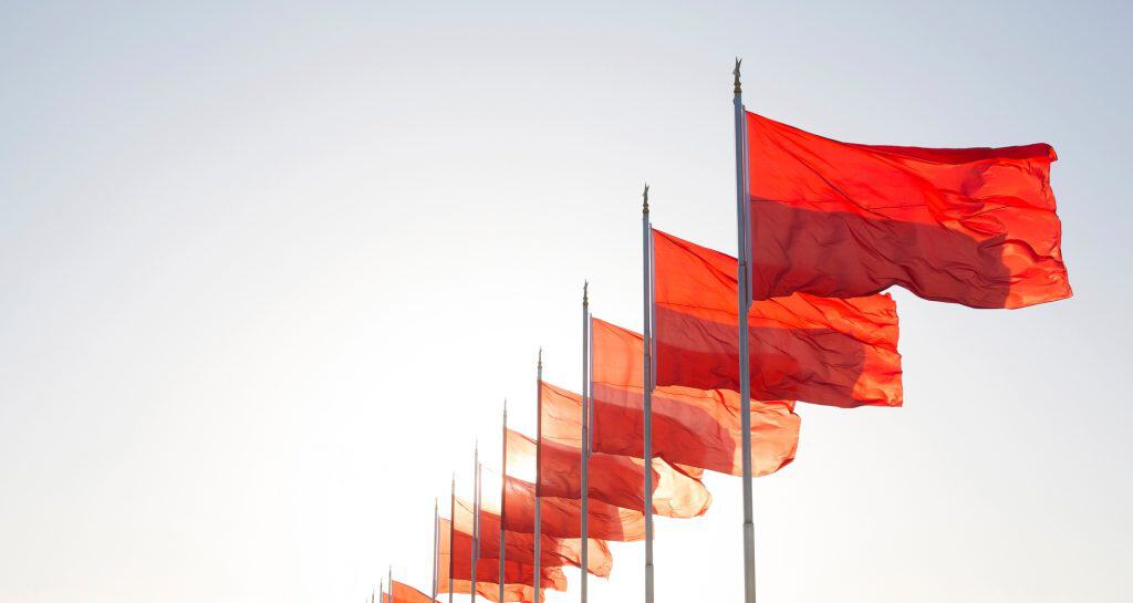Row of bright red flags on flagpoles fluttering in the wind, clear sky. represent red flags to watch for when choosing an seo agency